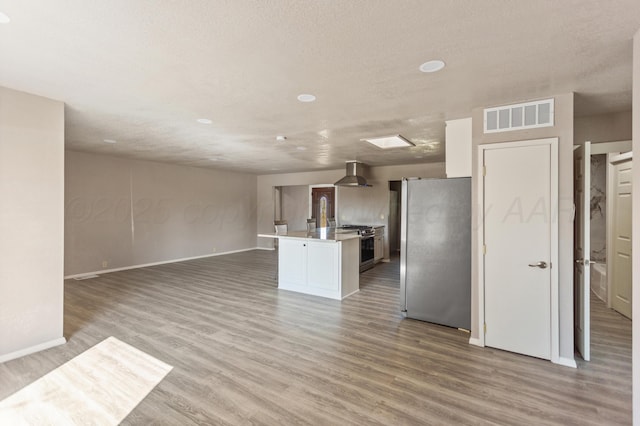 kitchen featuring light wood finished floors, wall chimney exhaust hood, open floor plan, stainless steel appliances, and visible vents