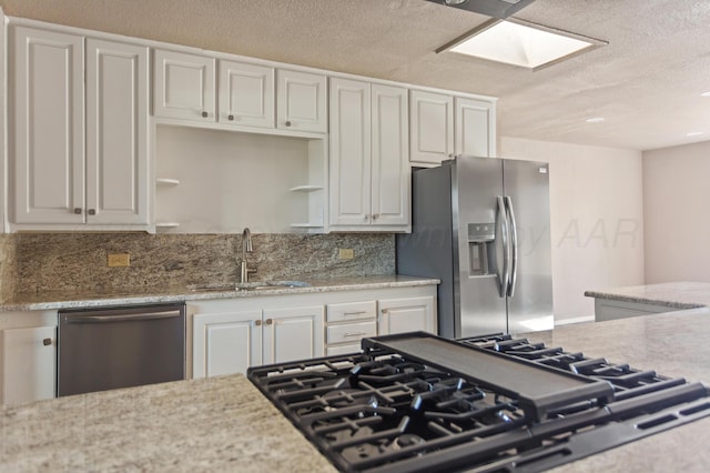 kitchen featuring a sink, white cabinetry, a textured ceiling, stainless steel appliances, and decorative backsplash