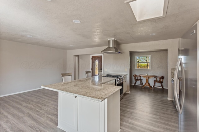 kitchen featuring wall chimney exhaust hood, wood finished floors, stainless steel appliances, and light stone counters