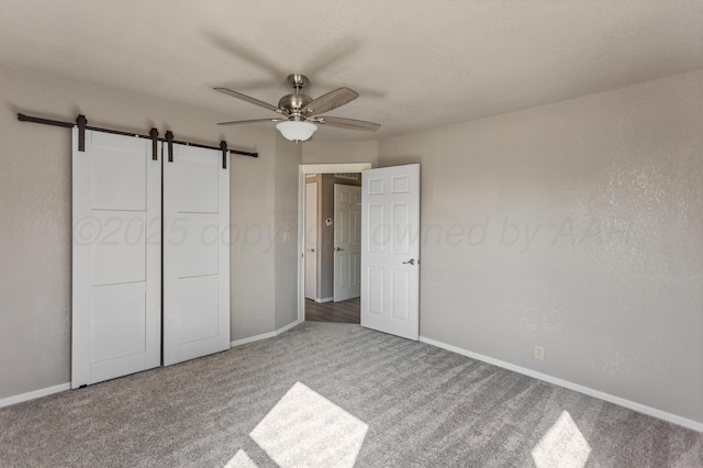 unfurnished bedroom featuring baseboards, a barn door, carpet, and a ceiling fan