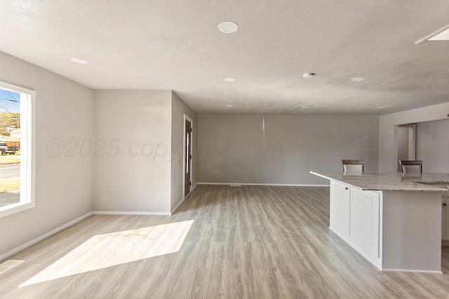 kitchen featuring a textured ceiling, white cabinetry, light wood-style flooring, and light stone counters