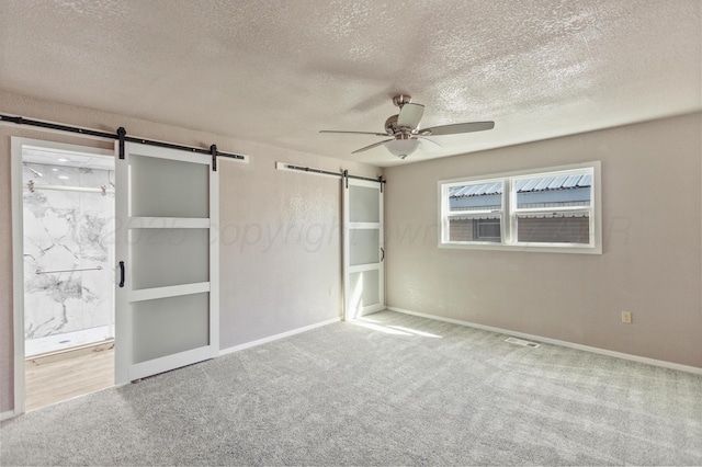 unfurnished bedroom featuring baseboards, a barn door, carpet floors, and ensuite bath