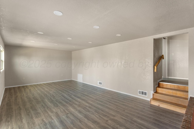 empty room featuring dark wood-style floors, visible vents, and stairway