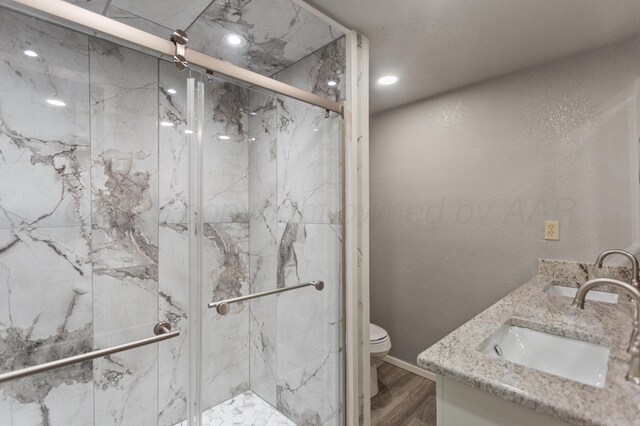 bathroom with toilet, a sink, a marble finish shower, wood finished floors, and double vanity
