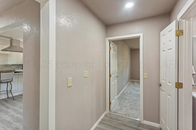 corridor with a textured wall, baseboards, and wood finished floors