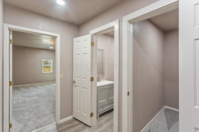 hall featuring baseboards, a textured ceiling, a sink, and light colored carpet