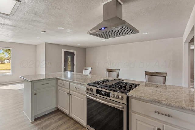 kitchen featuring island exhaust hood, light stone countertops, light wood-style flooring, and stainless steel gas stove