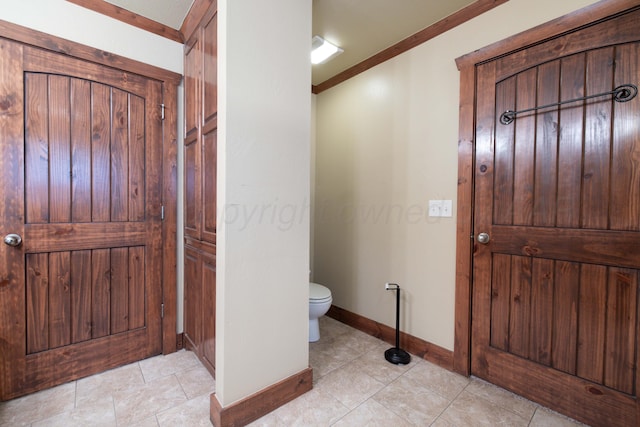 bathroom featuring tile patterned flooring, toilet, baseboards, and ornamental molding