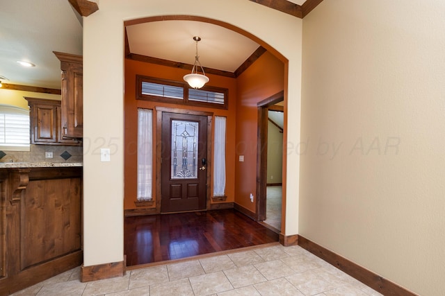 foyer entrance with arched walkways, crown molding, baseboards, and light tile patterned flooring