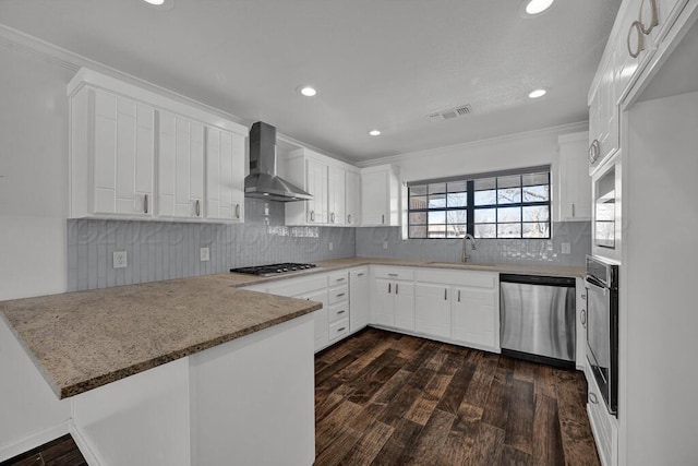 kitchen with stainless steel appliances, a peninsula, a sink, visible vents, and wall chimney range hood