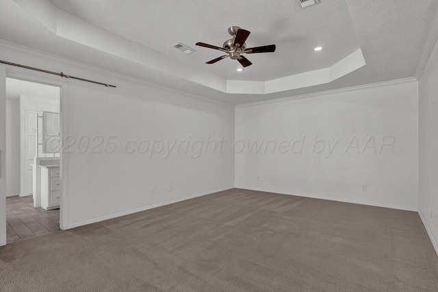 spare room featuring a raised ceiling, visible vents, a barn door, a ceiling fan, and carpet flooring