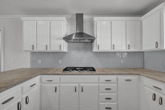 kitchen with light stone counters, stainless steel gas stovetop, backsplash, white cabinetry, and wall chimney exhaust hood