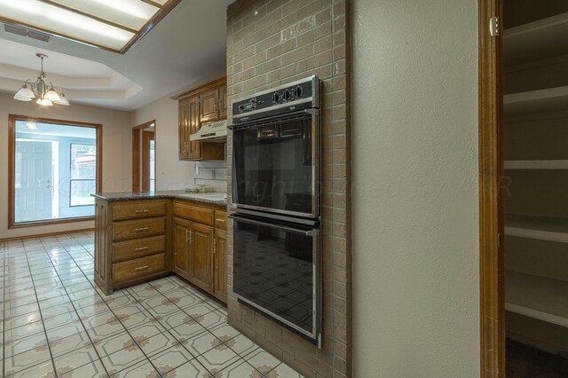 kitchen featuring kitchen peninsula, pendant lighting, double oven, a notable chandelier, and premium range hood