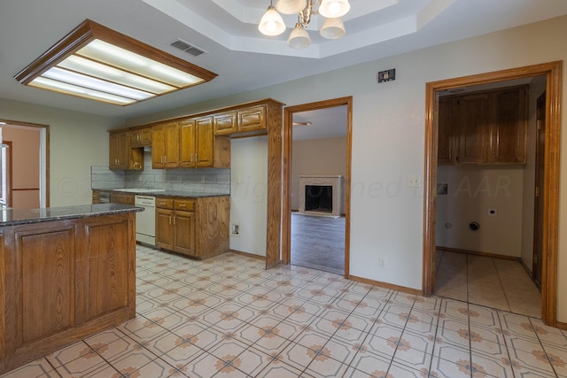 kitchen featuring dark stone counters, backsplash, a notable chandelier, white dishwasher, and a tray ceiling