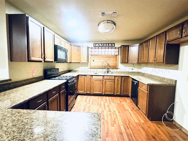 kitchen featuring light hardwood / wood-style flooring, black appliances, sink, and light stone counters