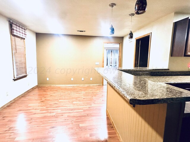 kitchen with light hardwood / wood-style floors, hanging light fixtures, sink, and dark stone counters