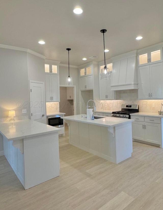 kitchen with stainless steel gas range oven, white cabinets, tasteful backsplash, and custom range hood