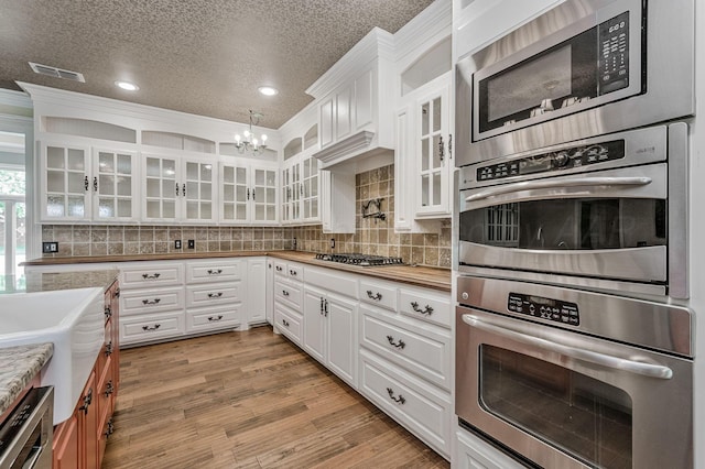 7723 Stuyvesant Ave, Amarillo, TX 79121 - kitchen featuring stainless steel appliances, white cabinets, a chandelier, a textured ceiling, and backsplash