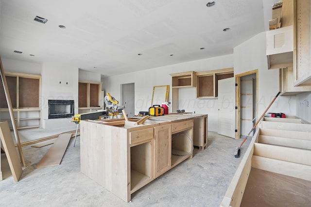 kitchen with a fireplace, a kitchen island with sink, and open shelves