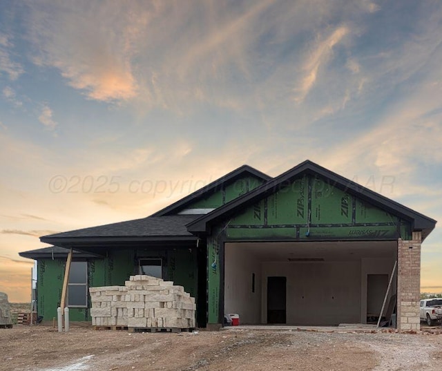 view of front of property with dirt driveway, an attached garage, and a shingled roof