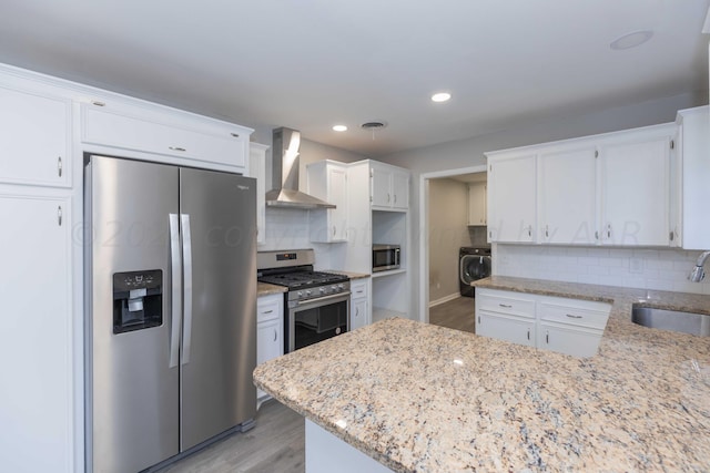 kitchen featuring wall chimney range hood, appliances with stainless steel finishes, washer / clothes dryer, sink, and white cabinets