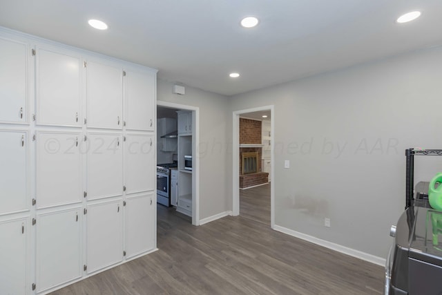 kitchen featuring dark wood-type flooring, a fireplace, stainless steel range with gas cooktop, and white cabinets