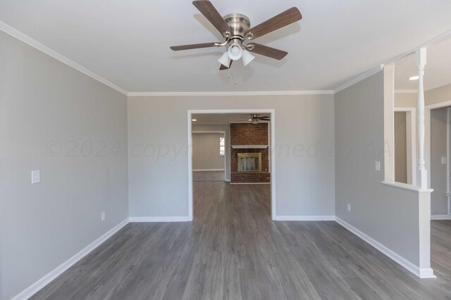 spare room with ornamental molding, a fireplace, dark wood-type flooring, and ceiling fan