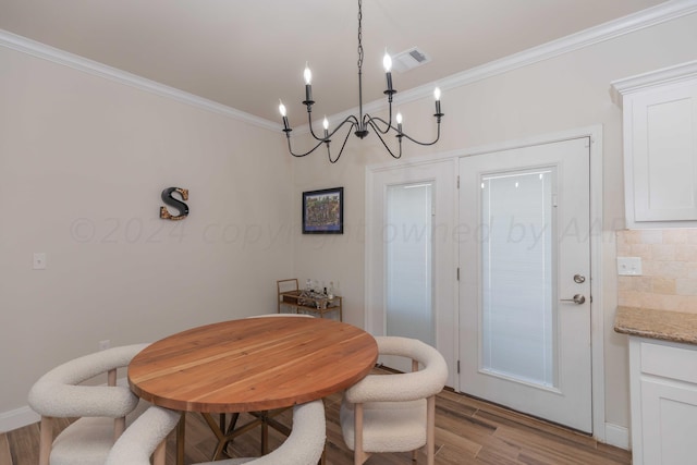 dining space with ornamental molding, visible vents, light wood-style flooring, and an inviting chandelier