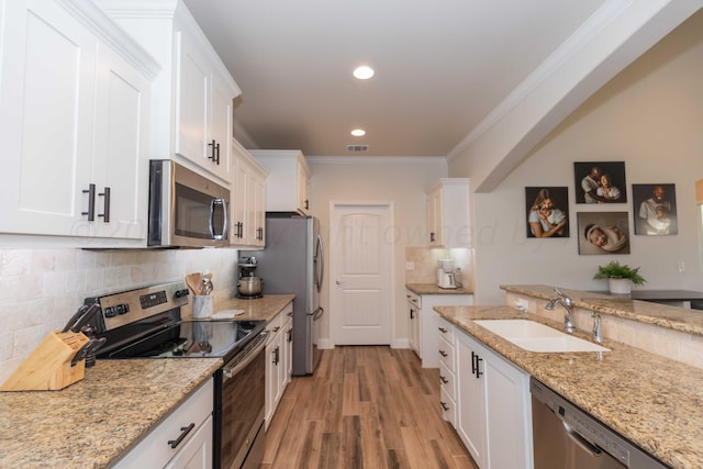 kitchen featuring a sink, ornamental molding, white cabinetry, light wood finished floors, and stainless steel appliances