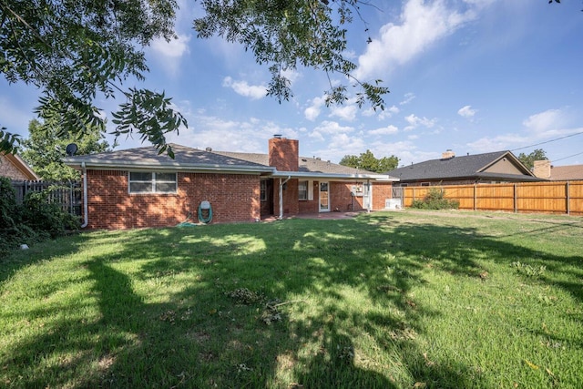 rear view of house featuring a chimney, brick siding, a fenced backyard, and a lawn