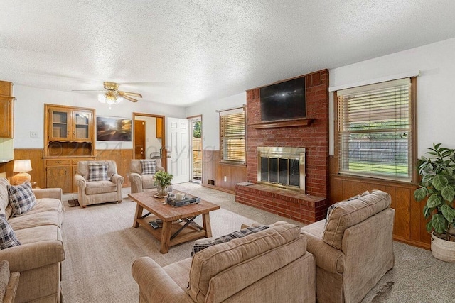 living area with ceiling fan, a textured ceiling, wooden walls, wainscoting, and light colored carpet