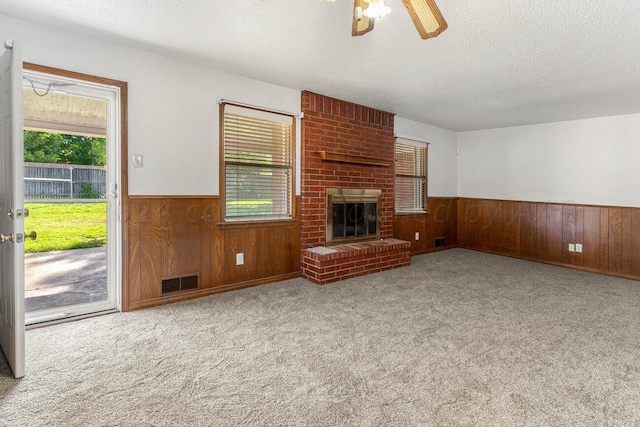 unfurnished living room featuring a textured ceiling, a ceiling fan, a wainscoted wall, wood walls, and visible vents