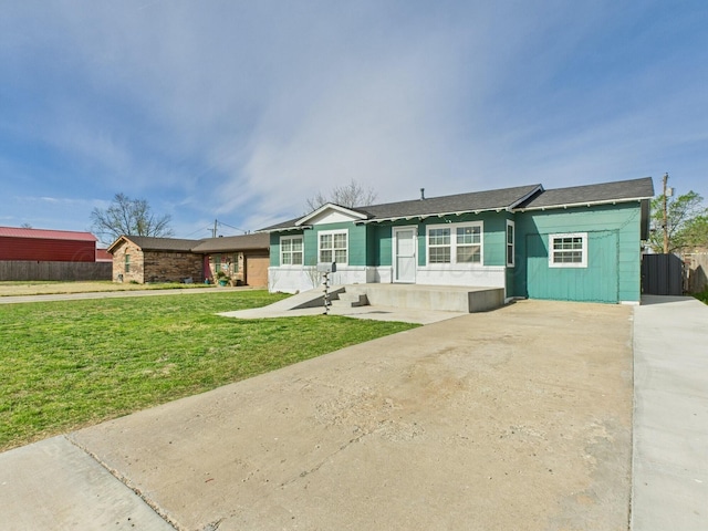 ranch-style home with concrete driveway, fence, and a front lawn