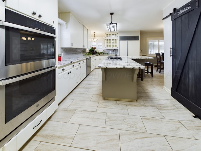 kitchen with tasteful backsplash, a barn door, decorative light fixtures, white cabinets, and a kitchen island