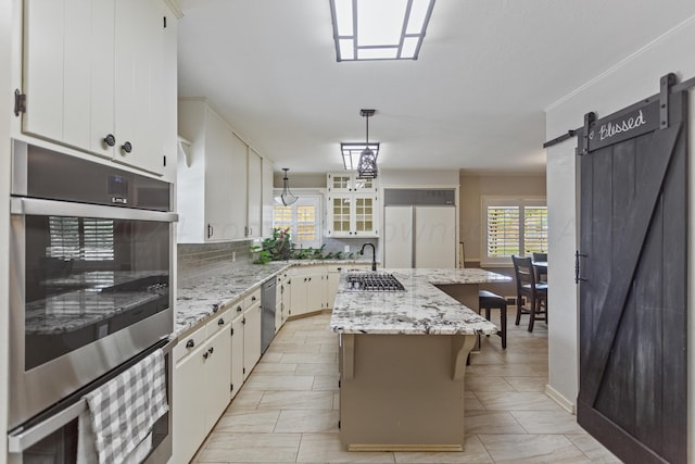 kitchen with appliances with stainless steel finishes, a barn door, decorative light fixtures, a center island, and white cabinetry