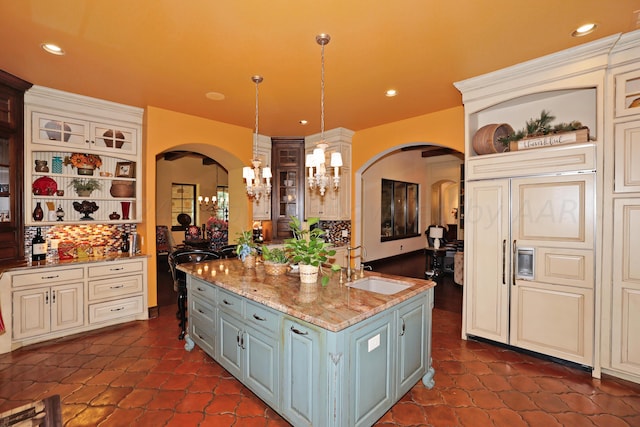 kitchen featuring a center island with sink, decorative light fixtures, stone countertops, gray cabinets, and decorative backsplash