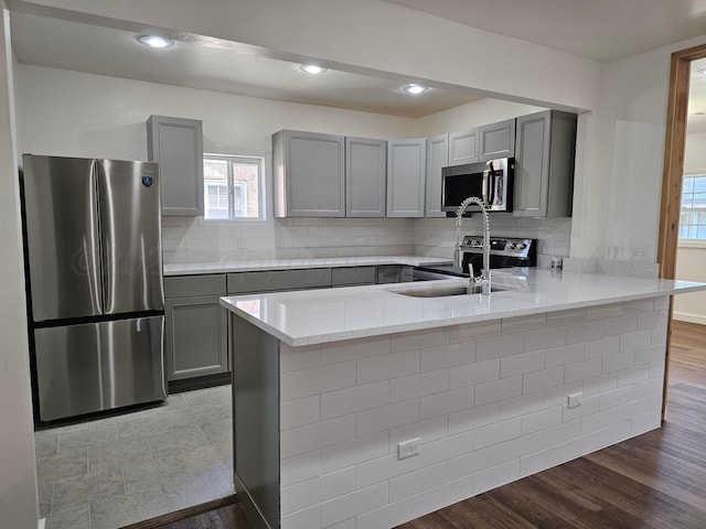 kitchen featuring a peninsula, light stone countertops, gray cabinetry, and appliances with stainless steel finishes