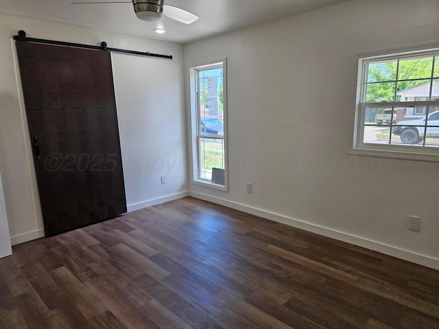 unfurnished bedroom with baseboards, multiple windows, a barn door, and dark wood-style floors