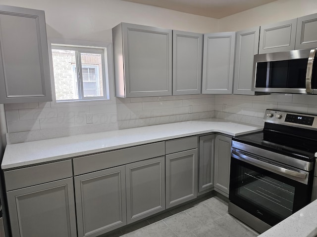 kitchen with gray cabinetry, stainless steel appliances, light stone countertops, and backsplash