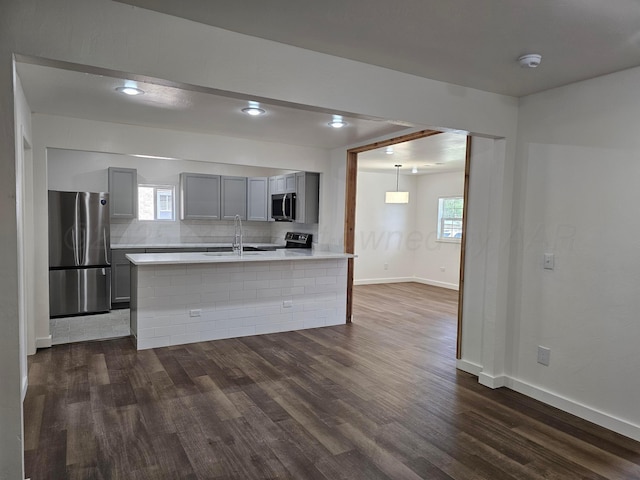 kitchen with stainless steel appliances, dark wood finished floors, light countertops, decorative backsplash, and gray cabinetry