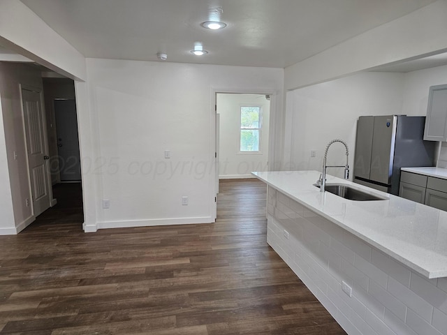 kitchen with freestanding refrigerator, light stone counters, a sink, dark wood-type flooring, and gray cabinets