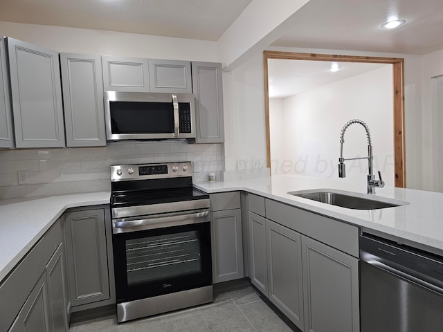 kitchen featuring gray cabinets, stainless steel appliances, decorative backsplash, and a sink