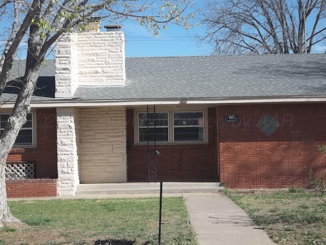 entrance to property featuring a chimney, a shingled roof, and brick siding