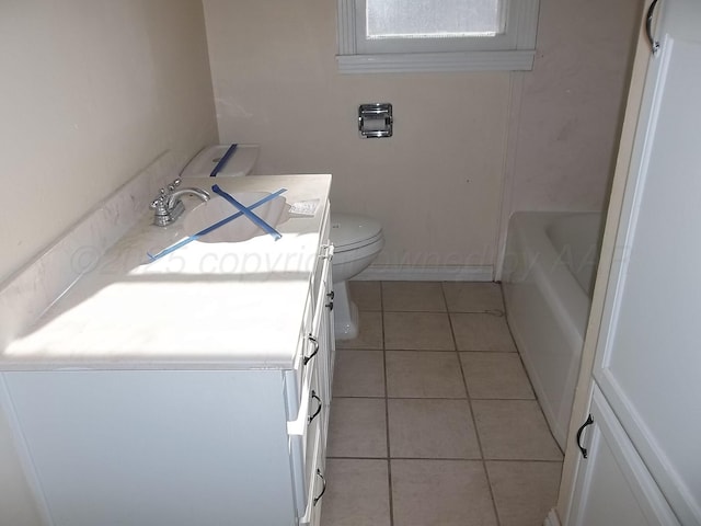 bathroom featuring toilet, vanity, tile patterned flooring, a bath, and baseboards