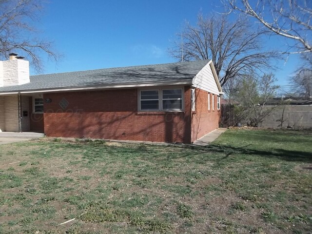 view of property exterior with a chimney, an attached carport, fence, brick siding, and a lawn