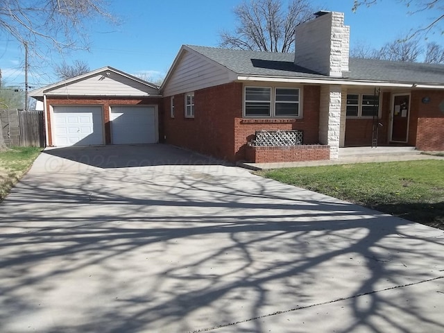 view of side of home with fence, an attached garage, driveway, brick siding, and a chimney