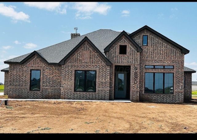 view of front of property featuring brick siding and roof with shingles