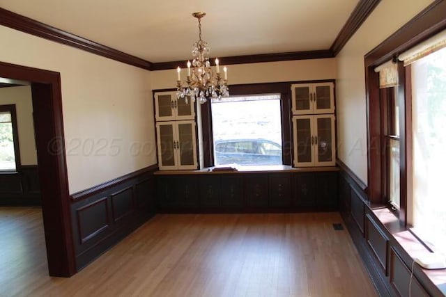 unfurnished dining area featuring crown molding, a notable chandelier, and wainscoting