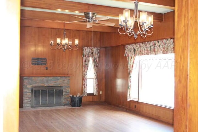 unfurnished living room featuring beamed ceiling, wood walls, ceiling fan with notable chandelier, a fireplace, and wood finished floors