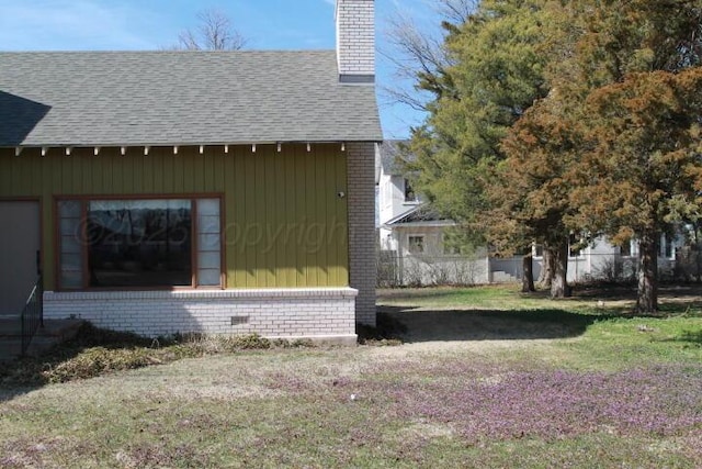 view of side of property with brick siding, a chimney, fence, and a shingled roof